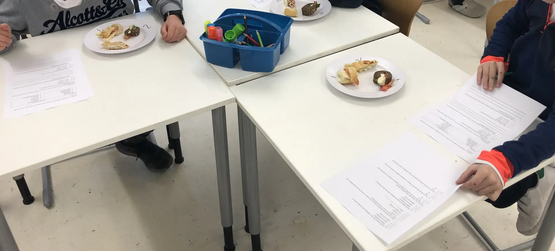Students taste-testing a mozzarella and tomato sandwich while filling out a self-created survey during a classroom business project.