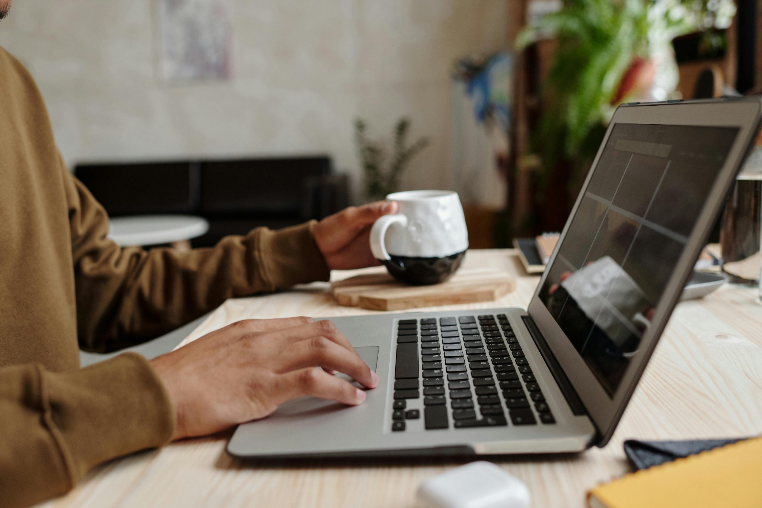 Teacher grasping a coffee mug while planning an authentic task on a laptop, illustrating the GRASPS model for authentic tasks.
