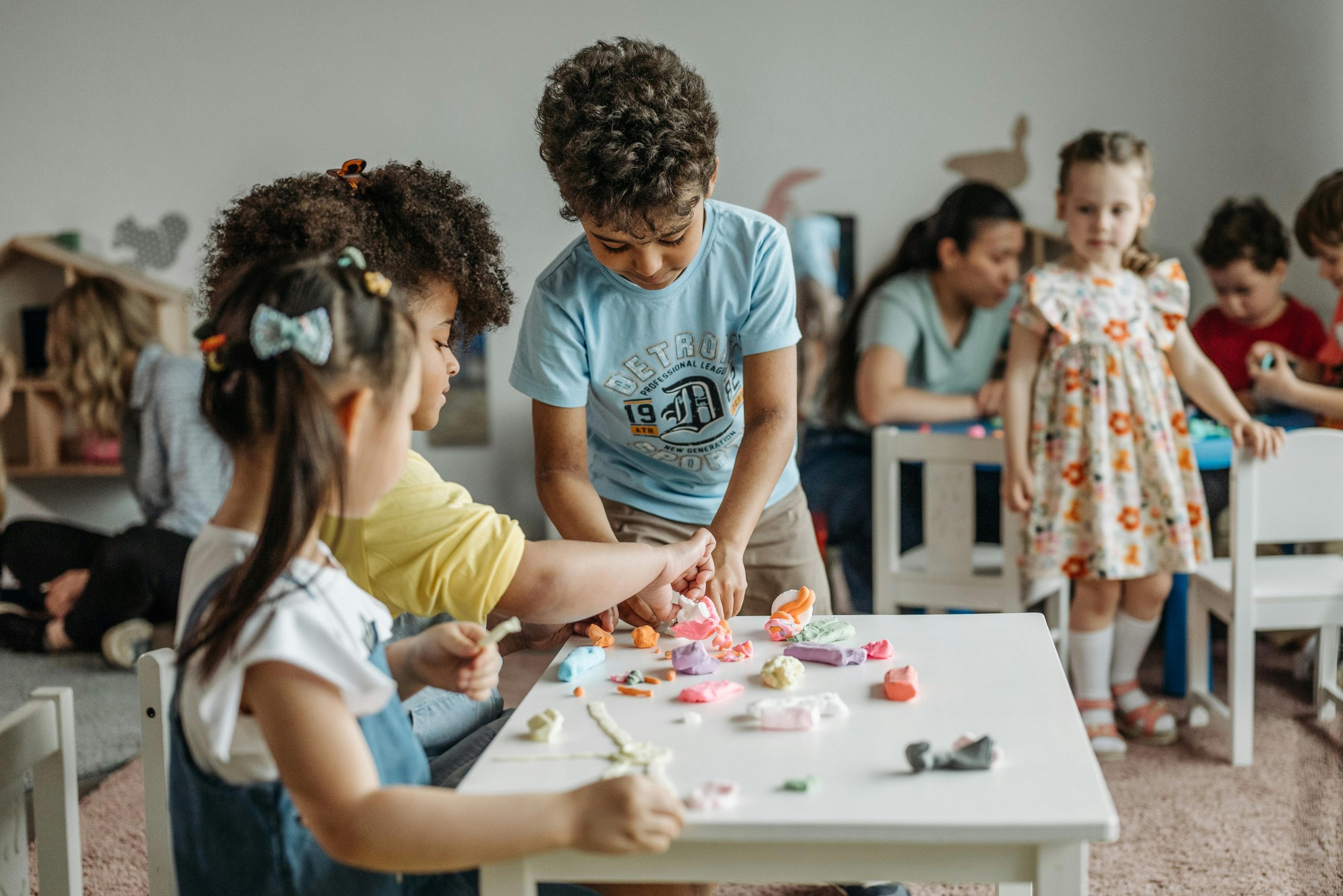 Children practicing social skills in the classroom while playing with colorful clay at a table.